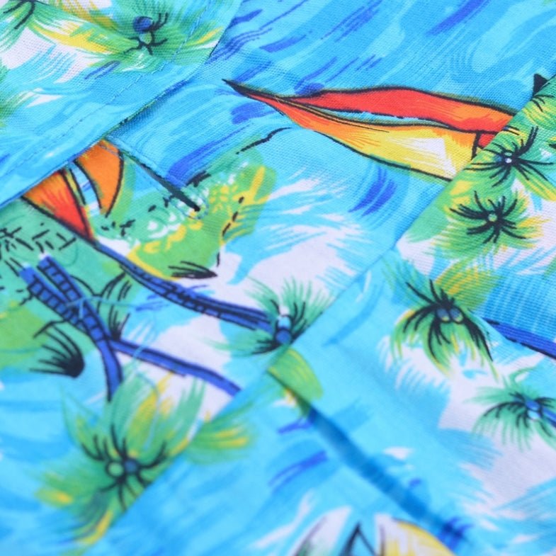 Close-up of light blue tropical fabric with surfboards, palms, and bird motifs