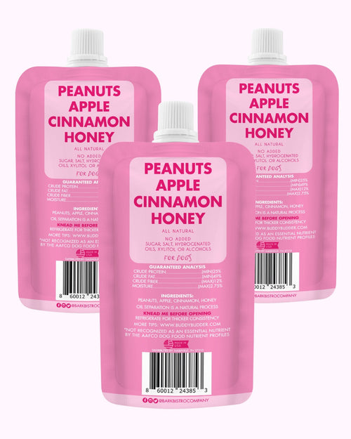Pink dog peanut butter squeeze pack pouches labeled Peanuts Apple Cinnamon Honey