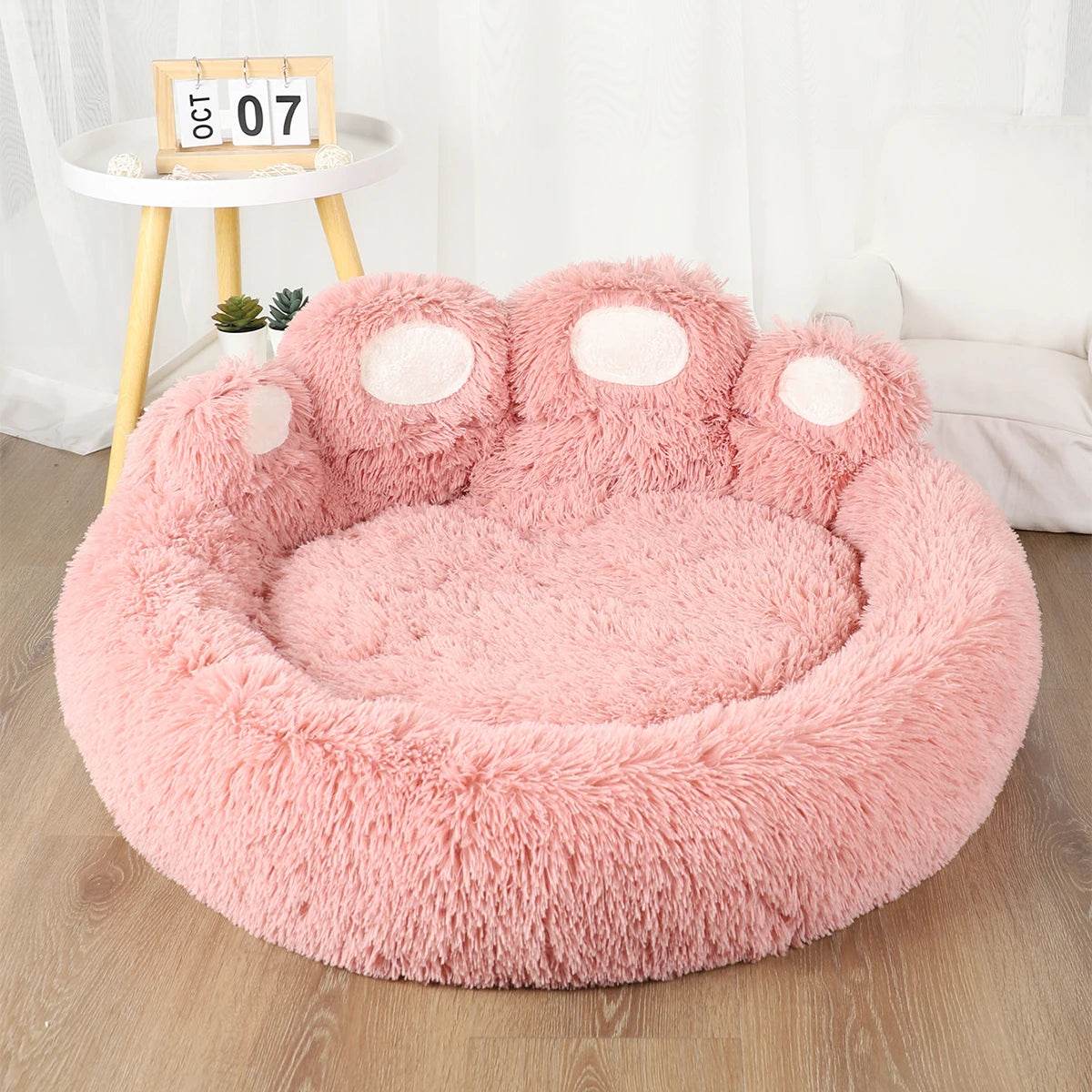 Pink round plush pet sofa bed with raised bolsters and paw-shaped accent pads