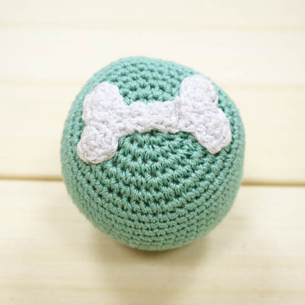 Teal crochet bone ball toy with white bone applique on the front.