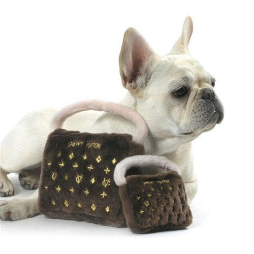 Plush squeaky dog toy bag with gold logo pattern, held by a white dog