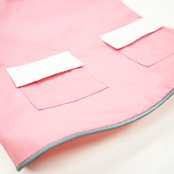 Pink dog raincoat fabric with white pocket flaps and dark trim edge, close-up
