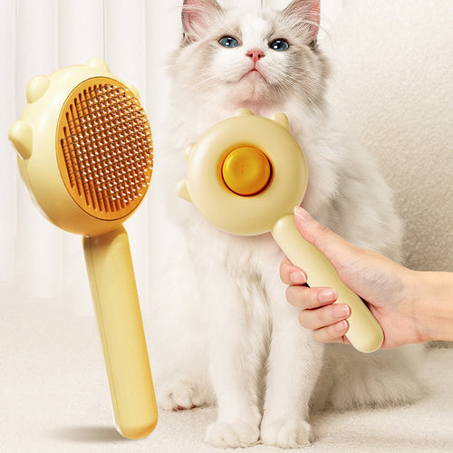 Yellow round massage pet brush with brown pin head, shown next to a white cat