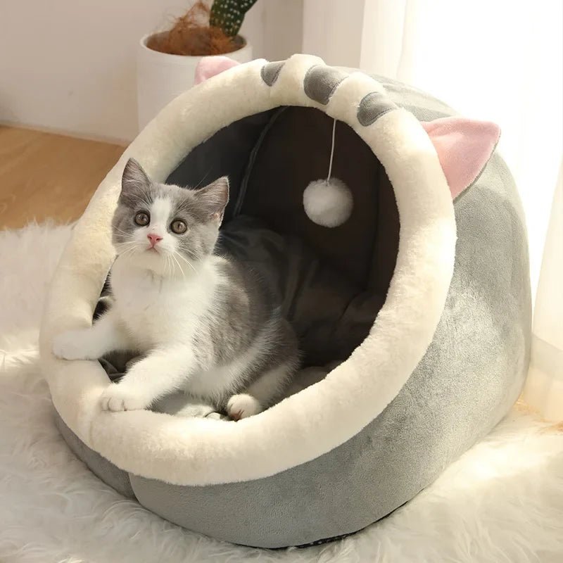 Plush cat cave bed with hanging ball toy, cream rim and dark interior, gray exterior