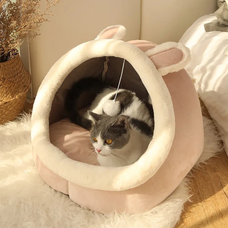 Plush cat cave bed with hanging ball toy, light beige rim and dark interior