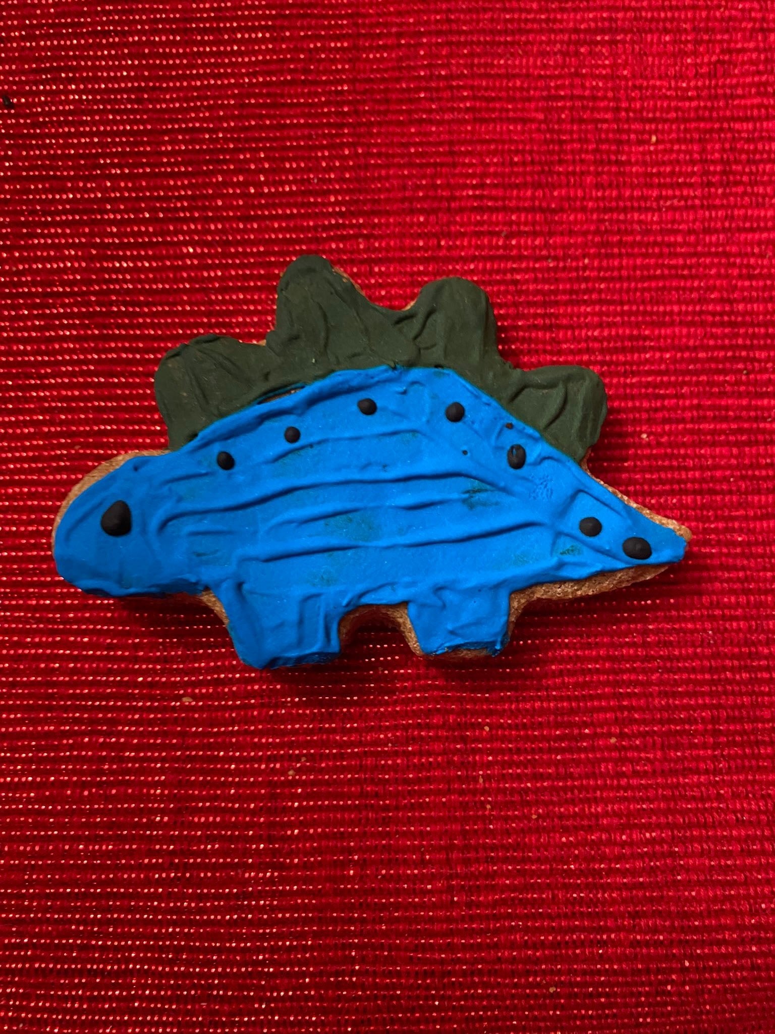 Blue stegosaurus-shaped dog cookie with dark spots and ridged back