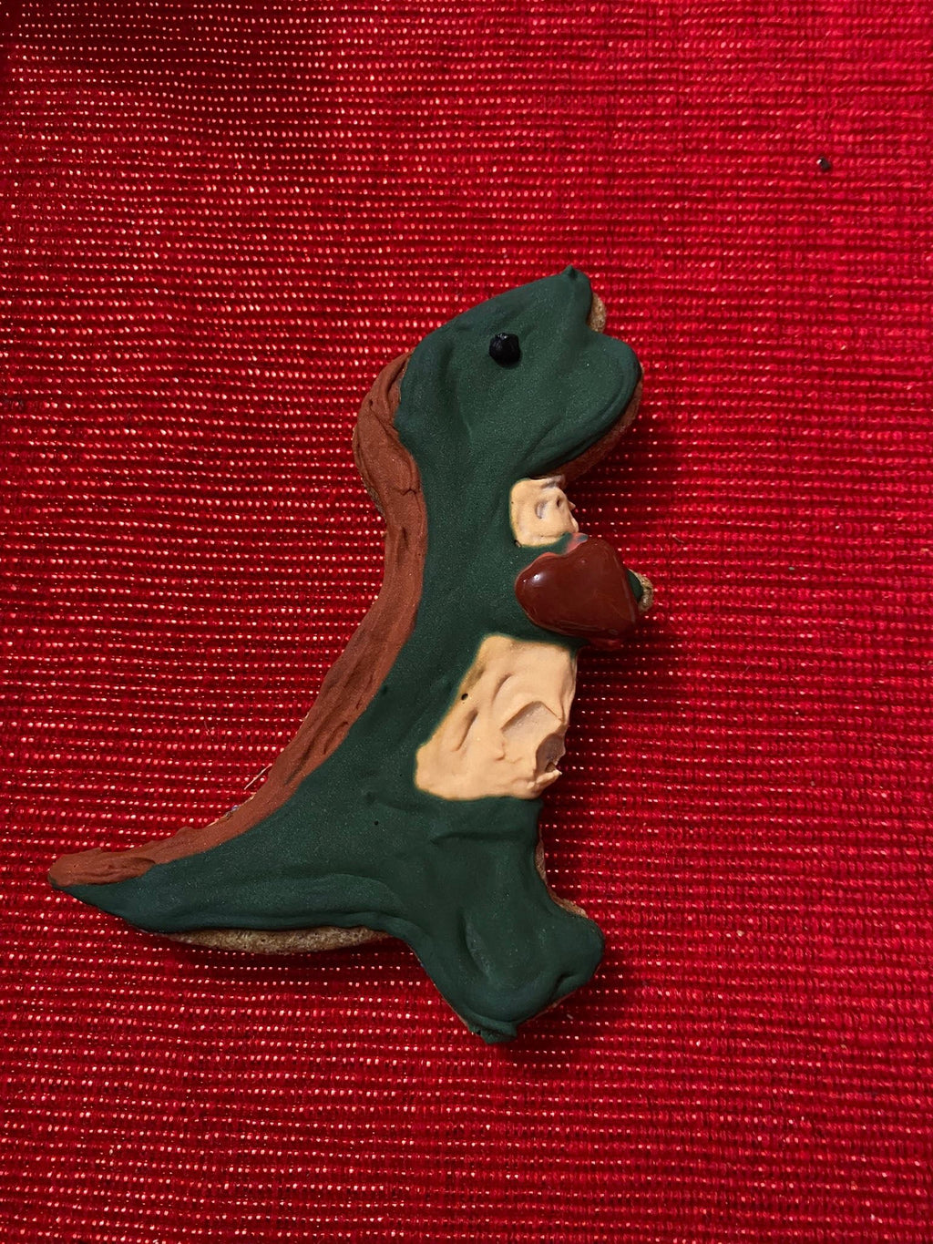 Green dinosaur-shaped dog cookie with small red heart and beige belly accents