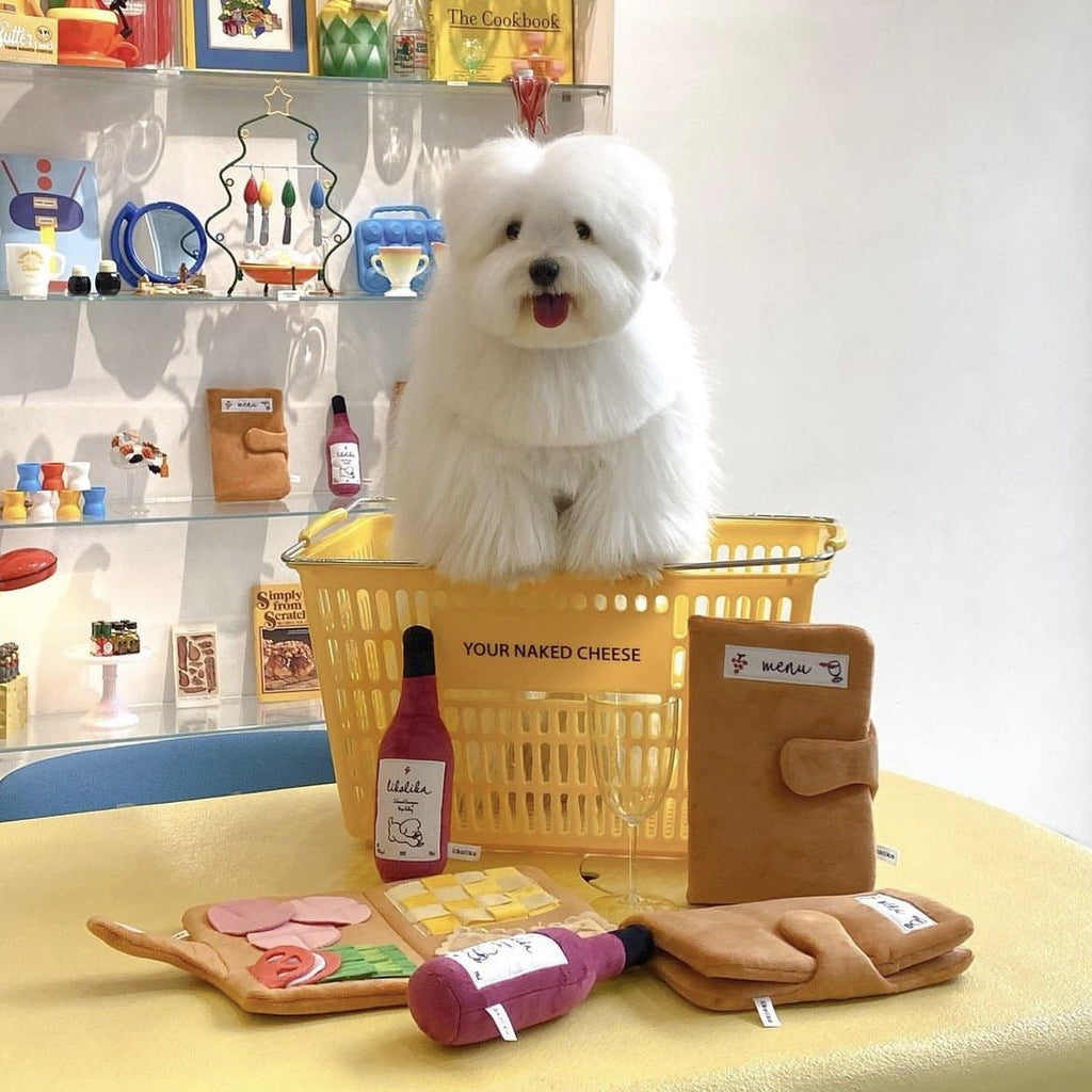 Dog with basket of plush puzzle smell pad toys, burgundy bottle, and treat shapes