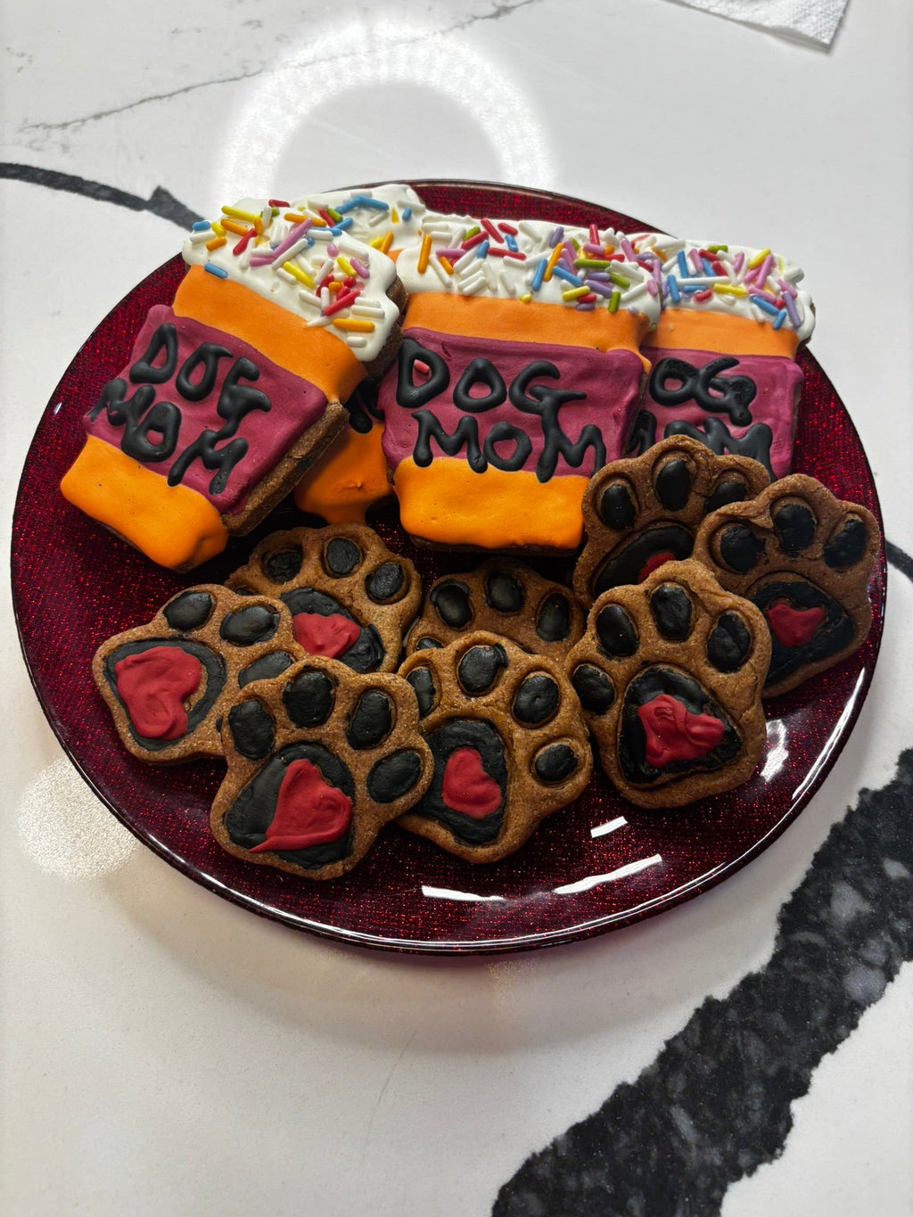 Dog paw and “Dog Mom” cookie assortment on a round plate, orange bones with sprinkles