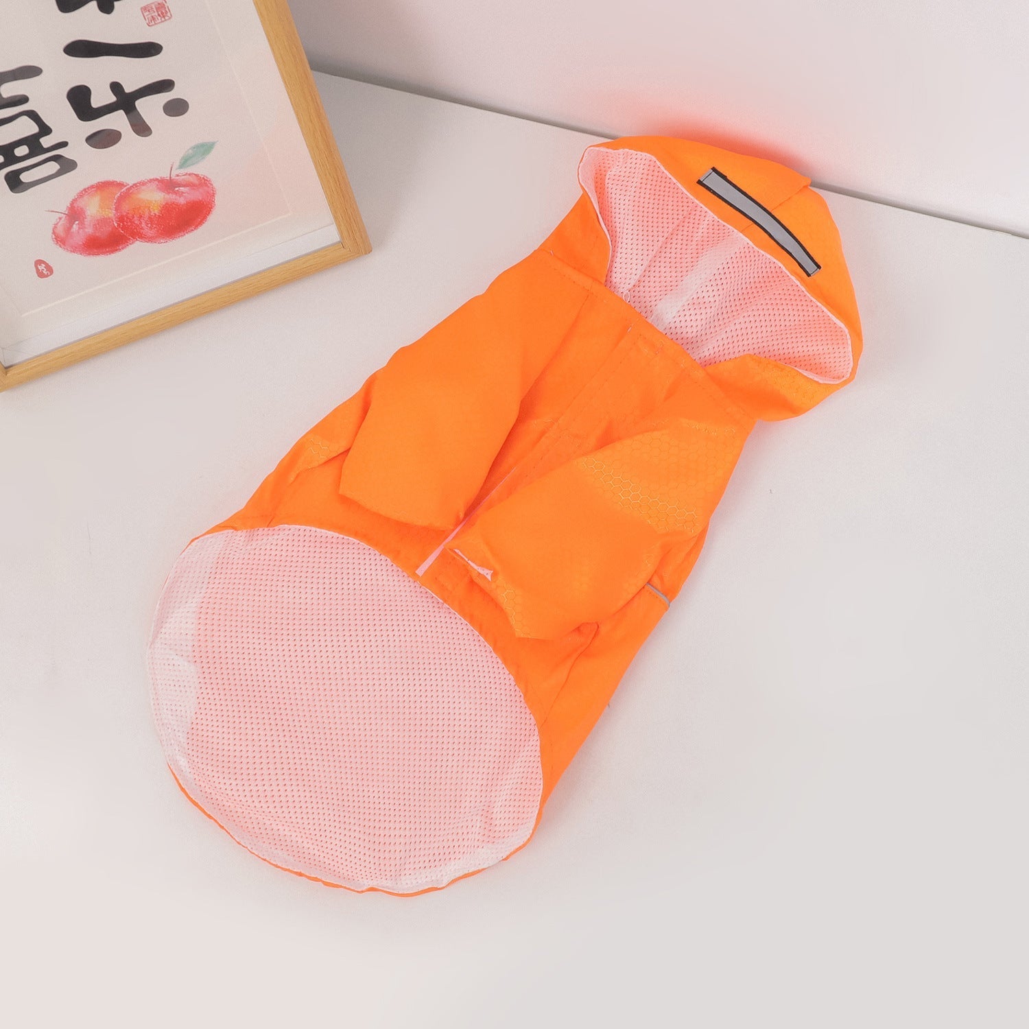 Orange dog raincoat with hood and mesh lining, with black strap detail on top.