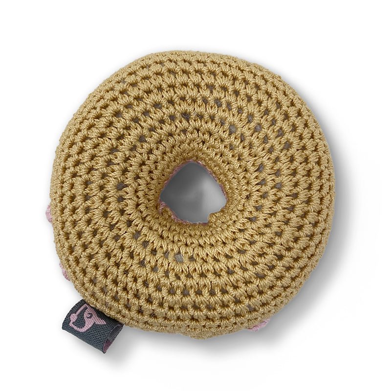 Crocheted tan donut toy with a stitched center hole and fabric brand tag