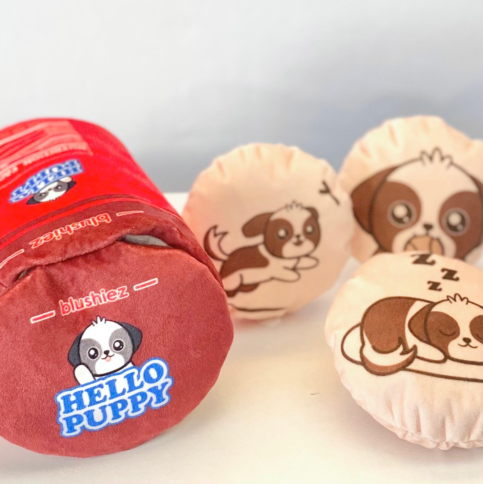 Close-up of red plush cylindrical dog toy and two beige round dog-face squeaky toys