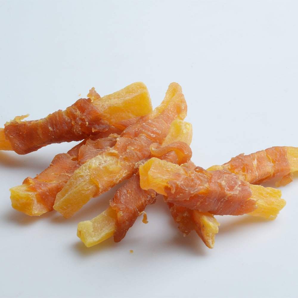 Chicken and sweet potato dog treat strips, orange and yellow pieces on a white background