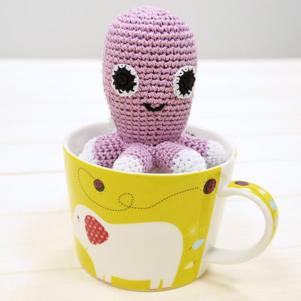 Lilac crocheted octopus plush with black eyes and open-mouth smile, white paw tips.