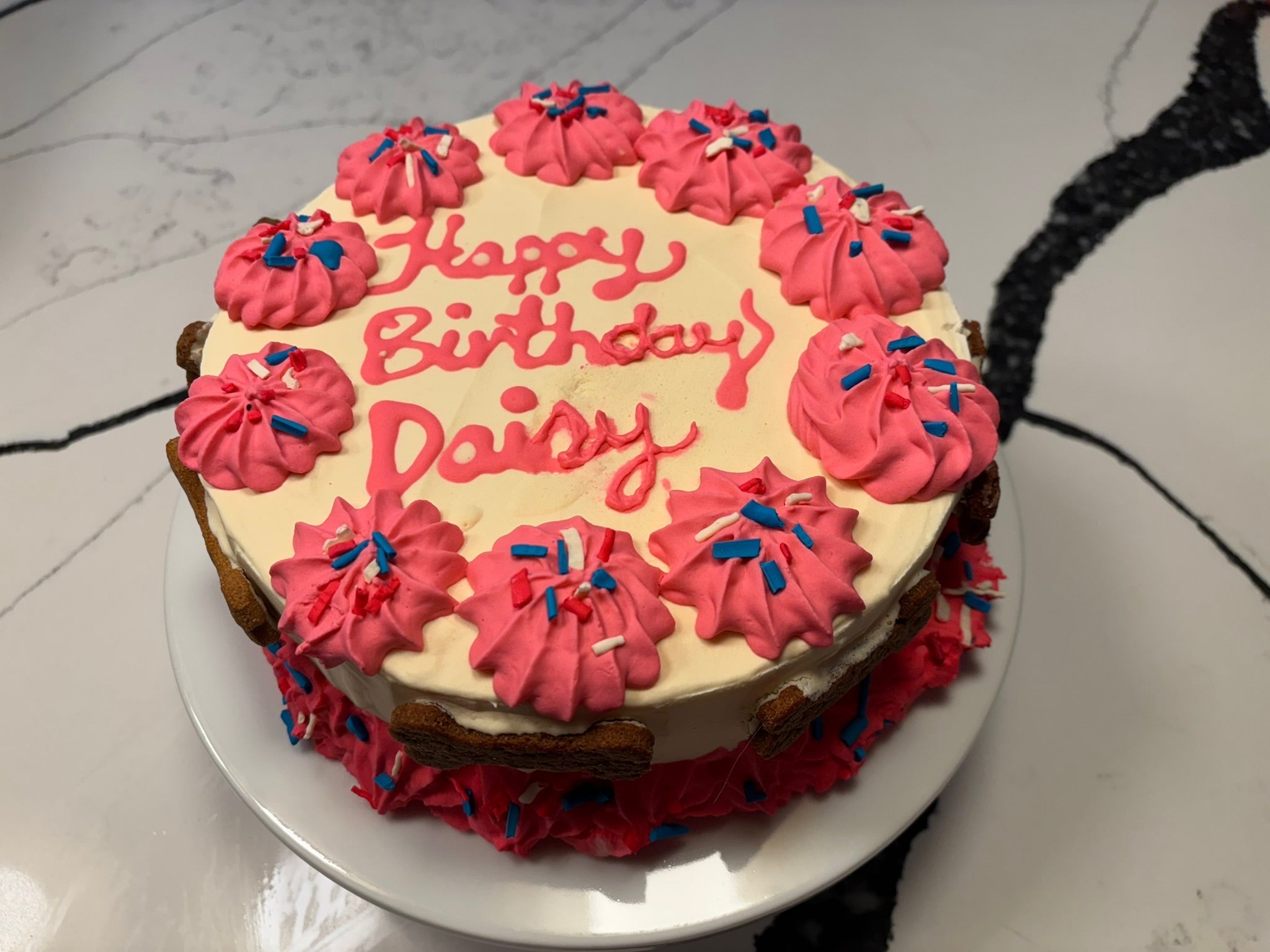 Top view of pink “Happy Birthday Daisy” cake with blue sprinkles and rosette frosting