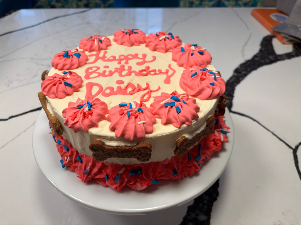 Round cream cake with pink rosette frosting and blue candy sprinkles around the edge