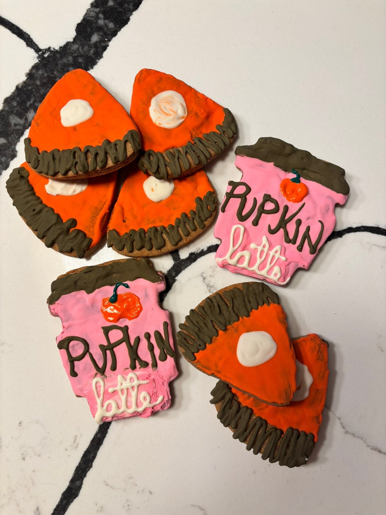 Assorted pumpkin-shaped dog cookies with orange tops, dark brown edges, and pink writing