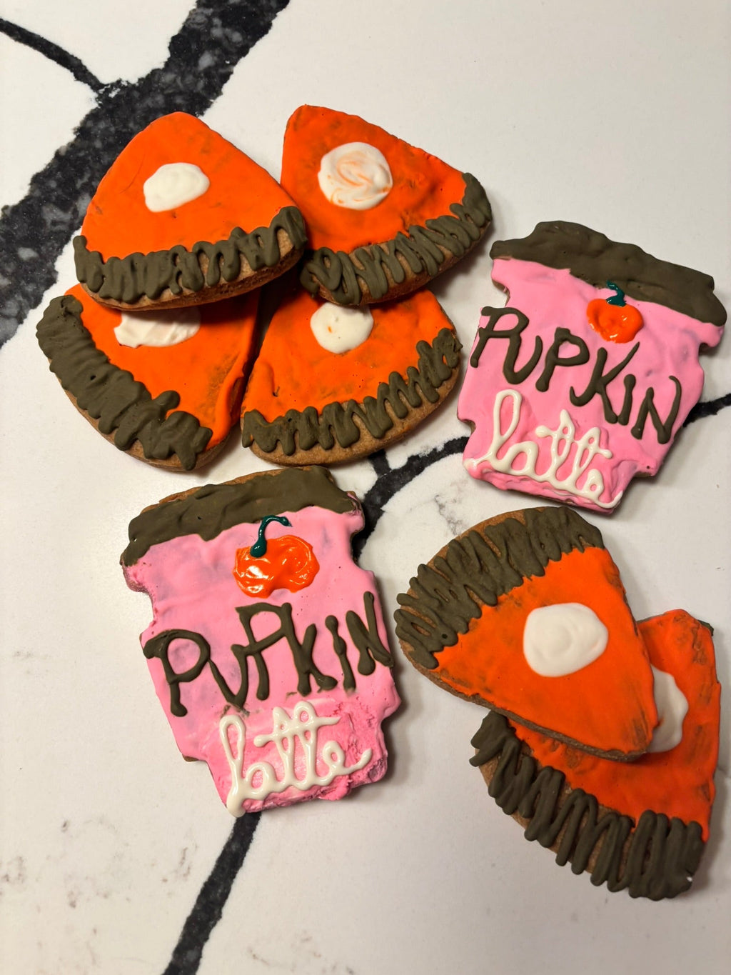 Assorted pumpkin-shaped dog cookies with orange, dark brown, and pink icing accents