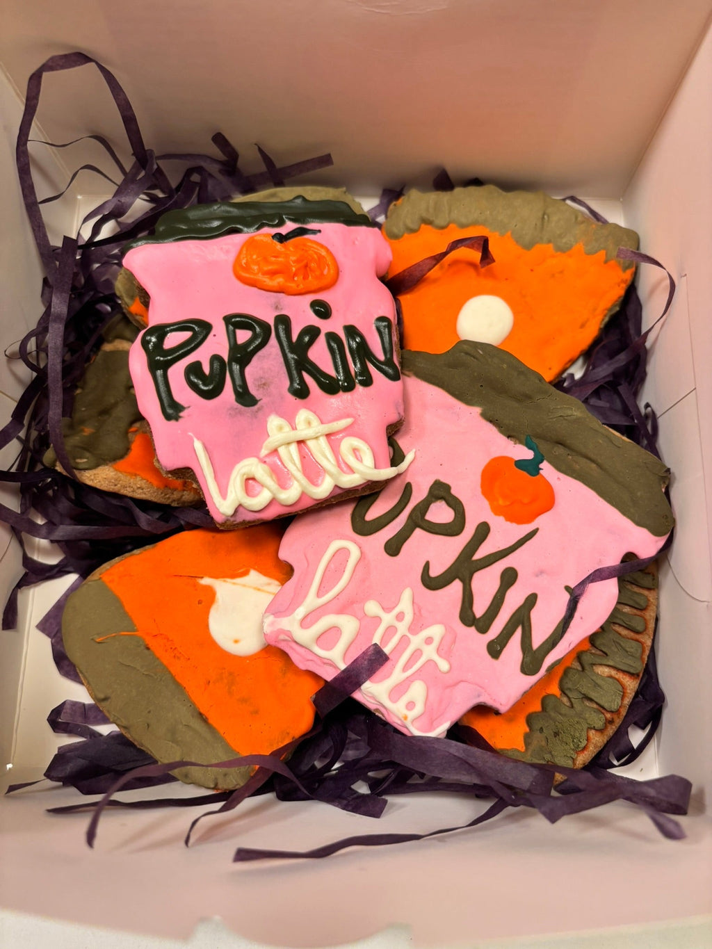 Packaged pumpkin-shaped dog cookies with pink icing and white dollops on purple filler