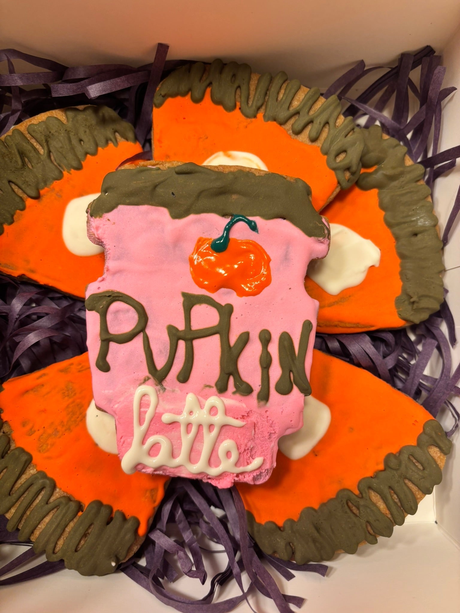 Pumpkin-shaped dog cookie with pink frosting, orange pumpkin details, and white icing