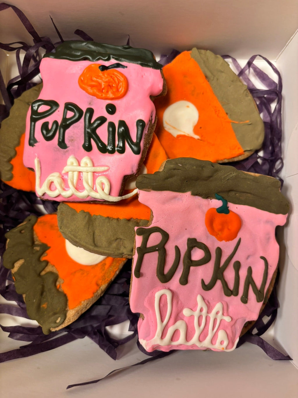 Set of pumpkin-shaped dog cookies with pink icing, dark brown tops, and white dollops