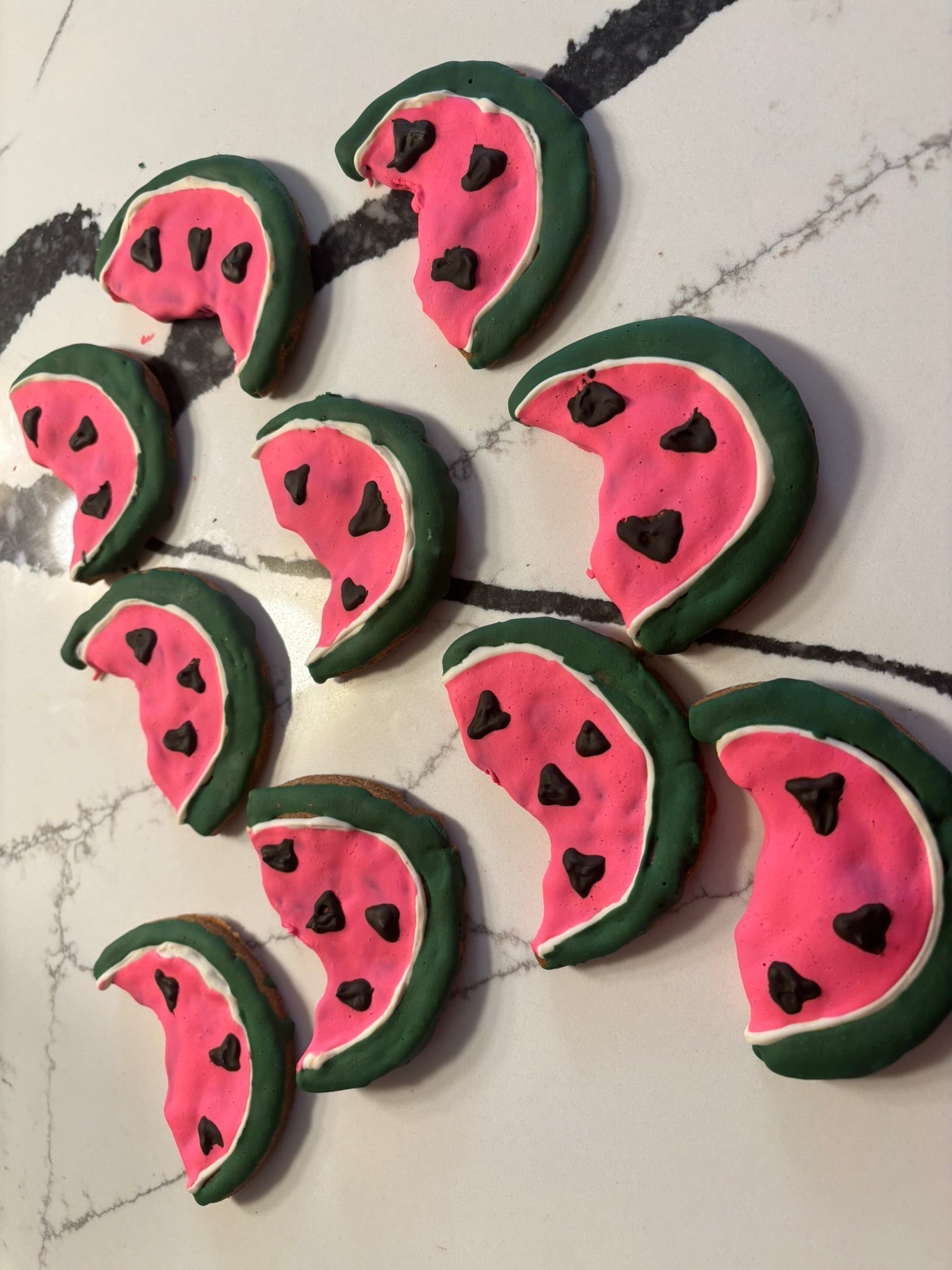 Assorted watermelon dog cookies scattered, pink centers with green rind and black seeds