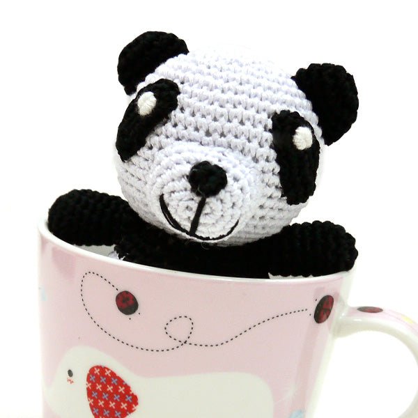 Crochet panda toy in a pink mug, black ears, stitched snout, and black arms.