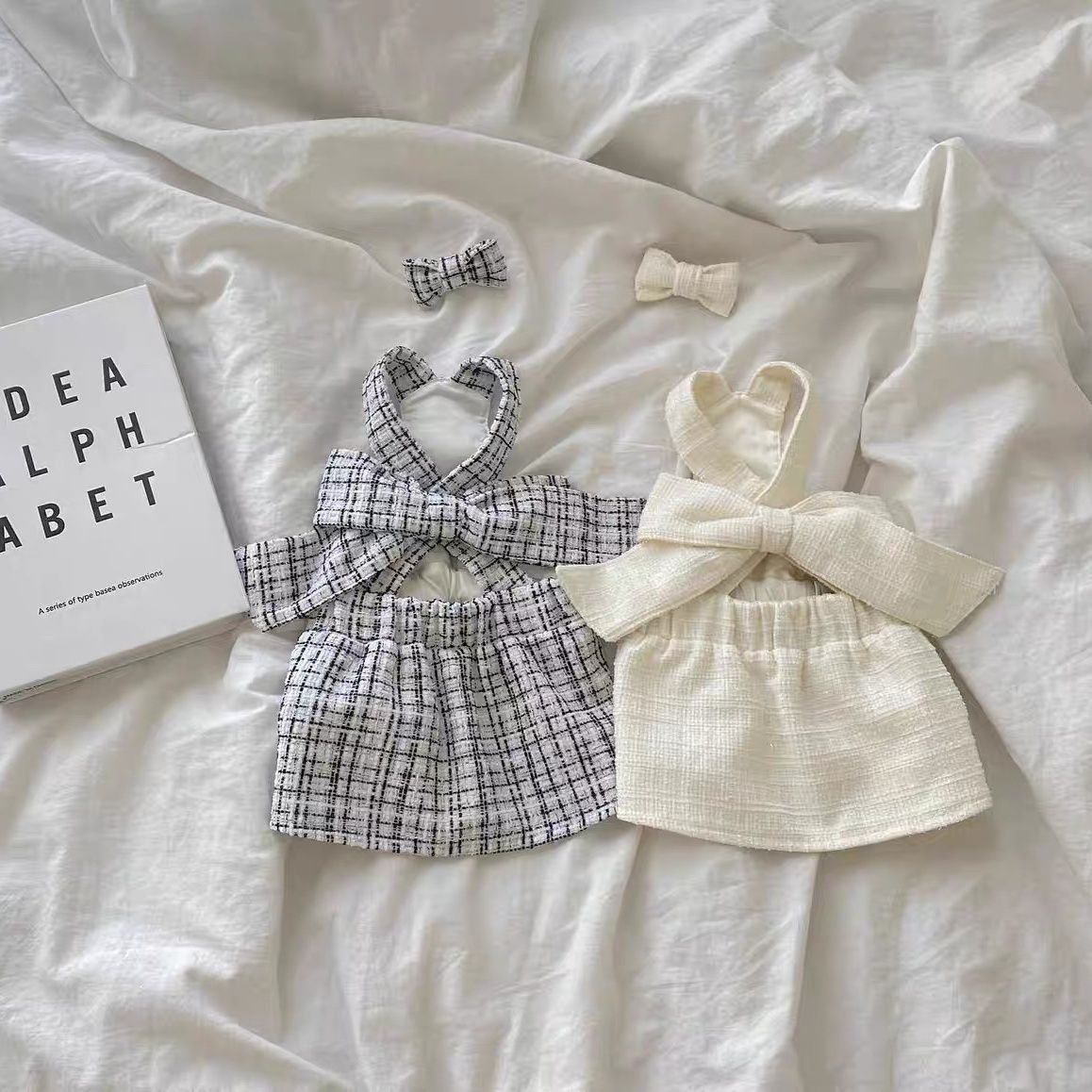Dog sling skirt dresses laid out: black-and-white plaid and cream with bows
