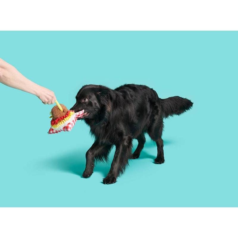 Black dog carrying stuffed red gingham scarf dog toy with brown meatball plush and yellow spaghetti
