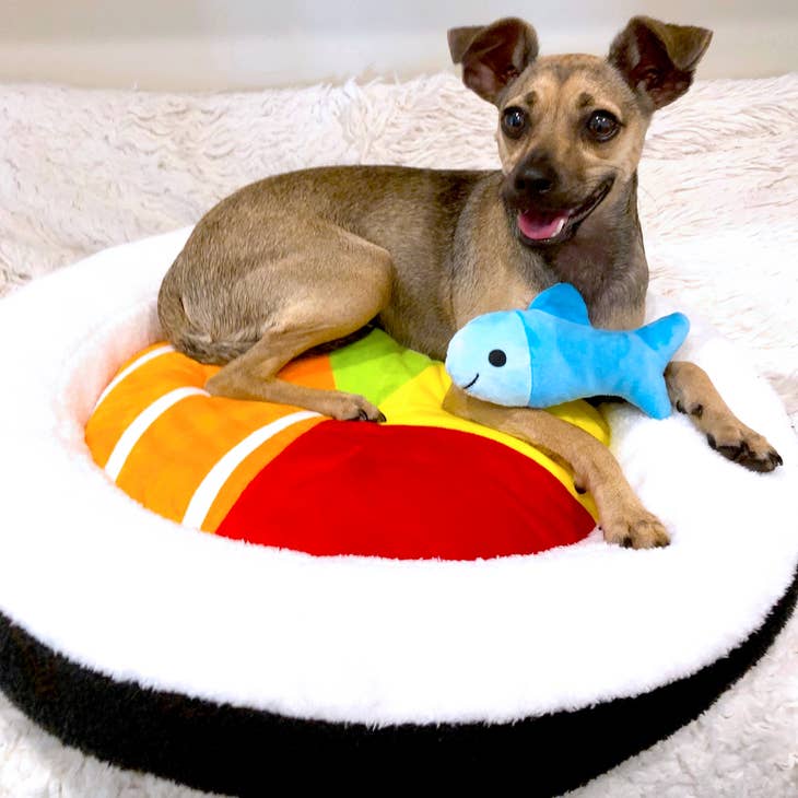 Round white plush pet bed with sushi roll insert; dog lying by blue fish crinkle toy