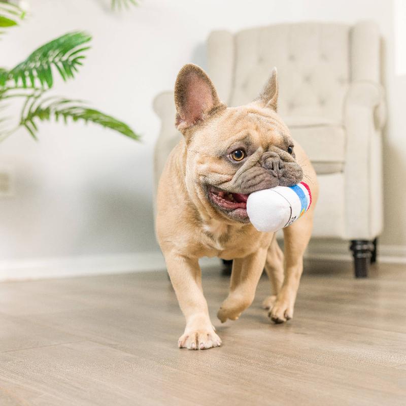 Plush dog toy in red, blue, and white held in a dog’s mouth