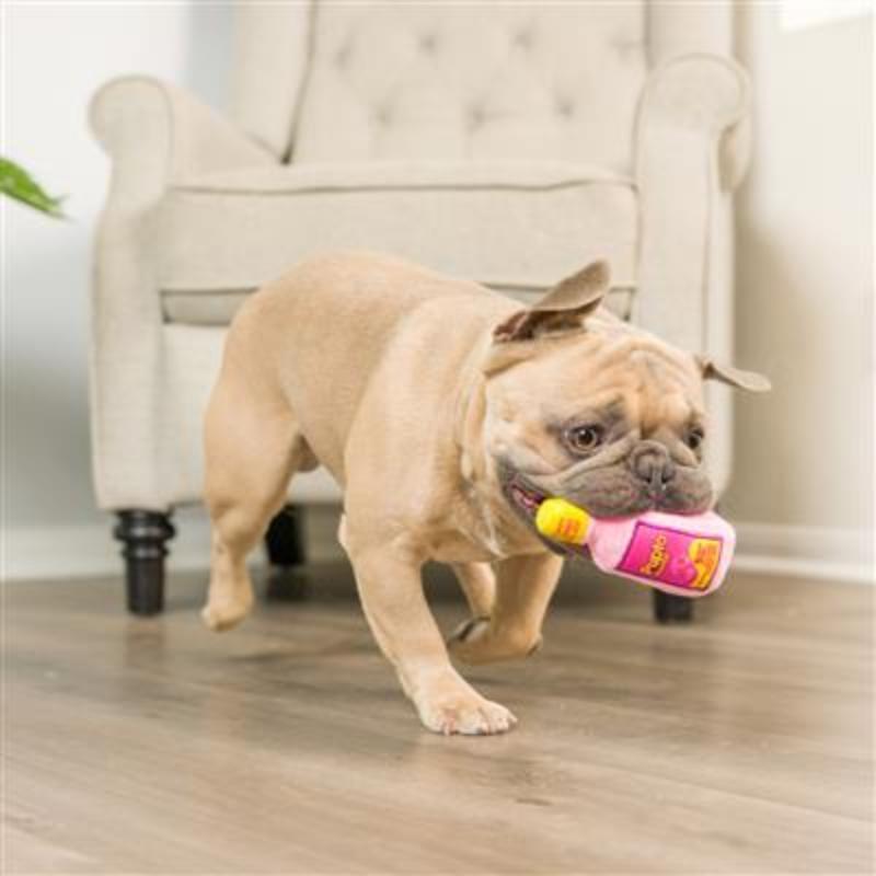 Pink bottle-style plush dog toy with colorful label, held in a bulldog’s mouth