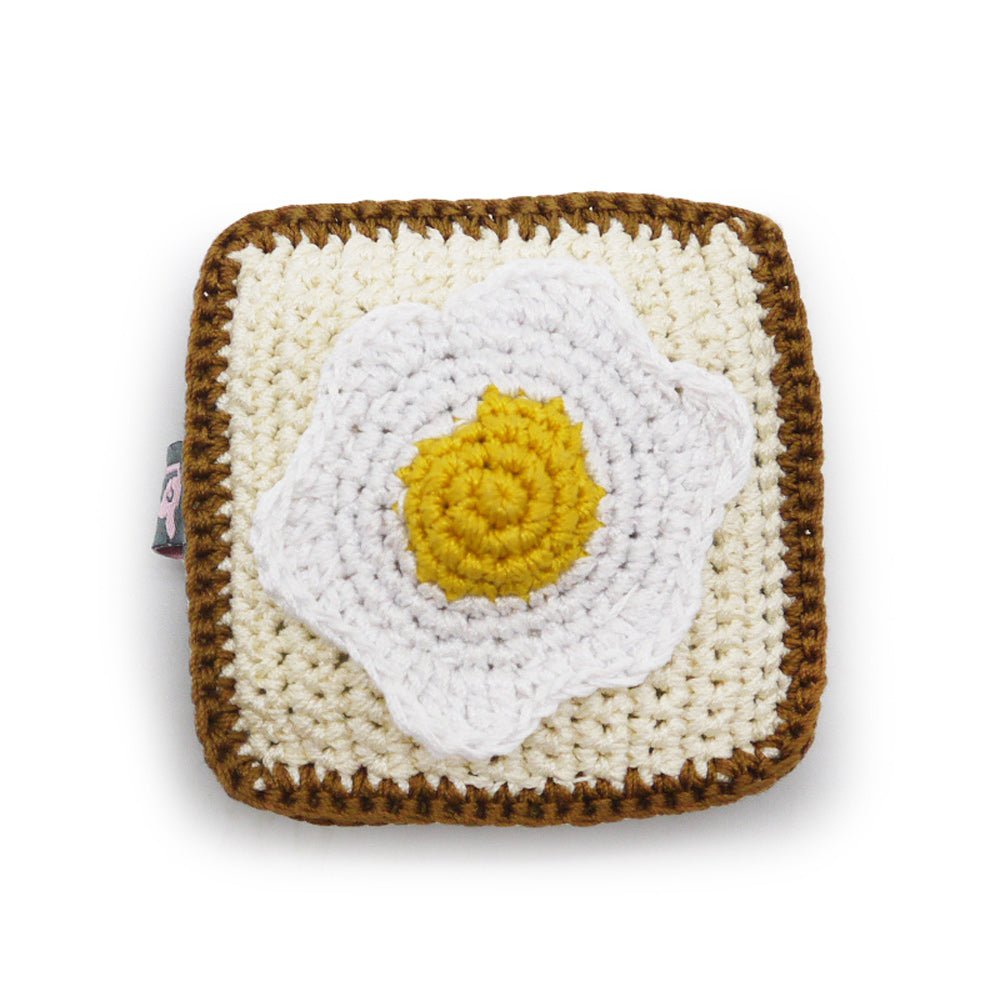 Crochet toast toy with large white egg and yellow yolk on cream square, brown trim