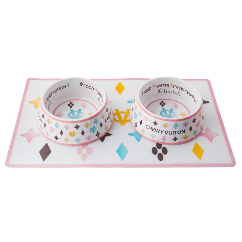 Two white pet bowls with “CHEWY VUITON” graphics on a pink matching mat